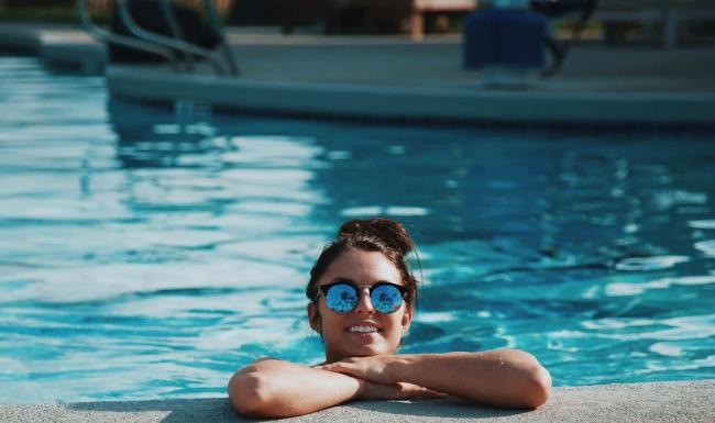 Sparkling swimming pool woman with sunglasses, in a pool, rests her arms on the ledge and smiles