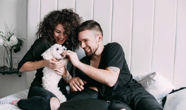 We love our furry friends a man and woman sitting on a bed playing with a dog